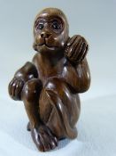 Japanese carved wood Netsuke - In the form of a seated monkey with glass eyes holding nuts, having a