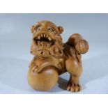 Japanese carved wooden Netsuke depicting a dragon with one foot astride a ball.