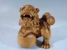 Japanese carved wooden Netsuke depicting a dragon with one foot astride a ball.