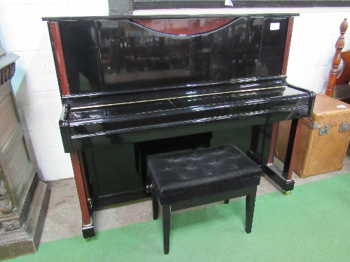 A Hemmington upright piano in gloss black finish with dark brown embellishments, on casters. Frame