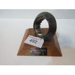 Manor Formula 1 racing team competition wheel nut mounted on a wooden plinth. Estimate £20-40.