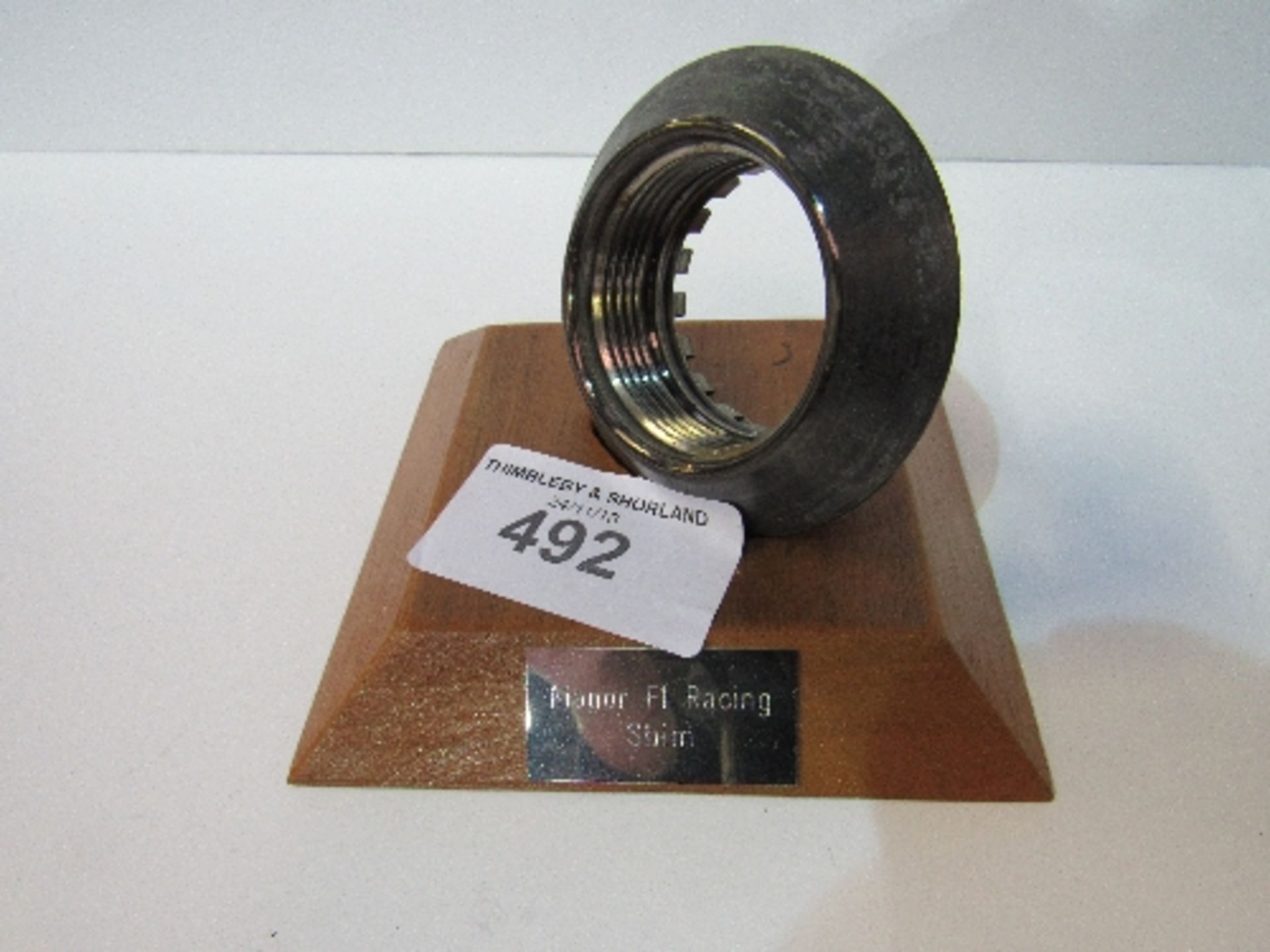 Manor Formula 1 racing team competition wheel nut mounted on a wooden plinth. Estimate £20-40.