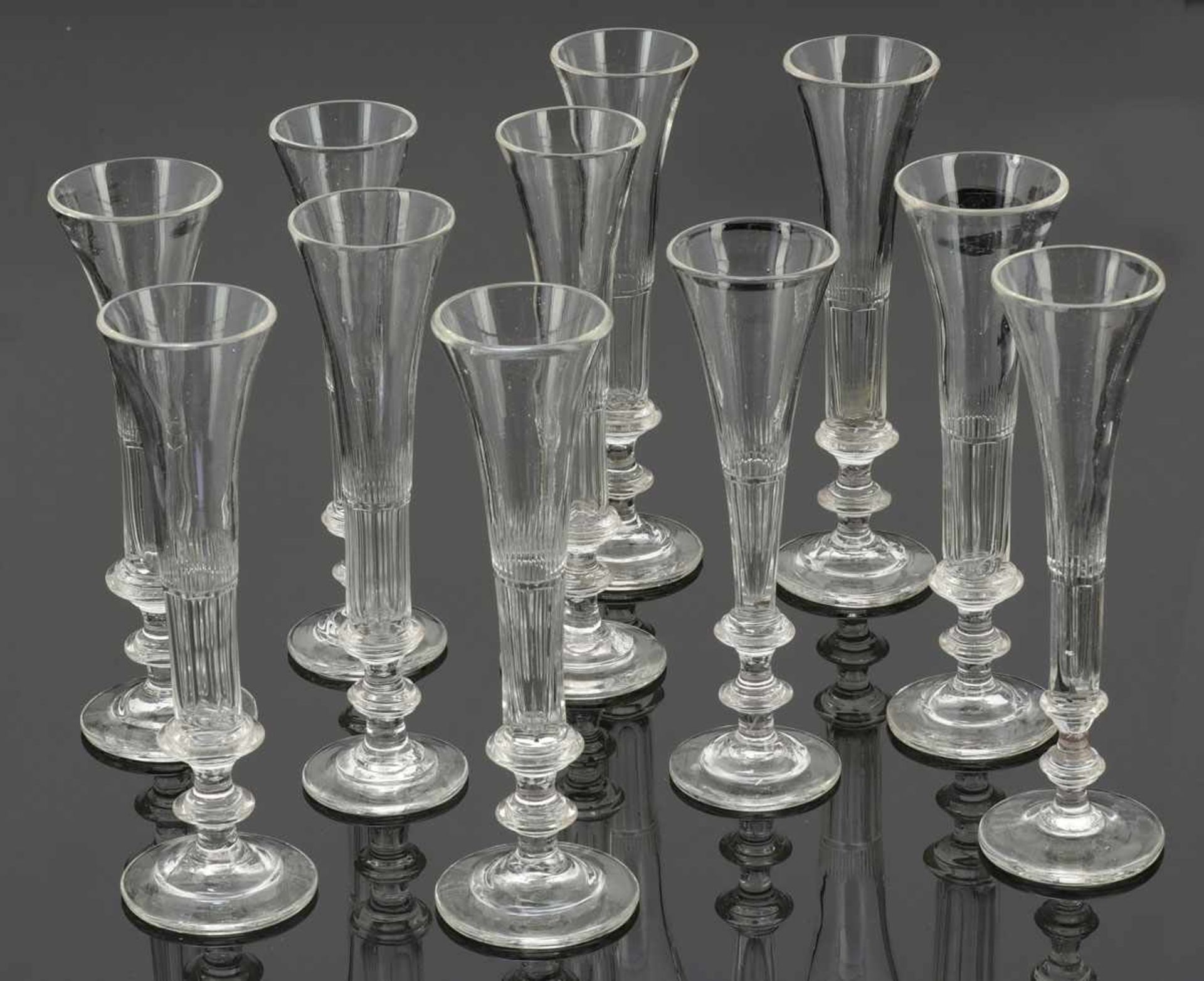 11 Sektflöten Mitte 19. Jh. Farbloses Glas, facettiert. H. bis 21,5 cm. Getreppter Scheibenfuß.