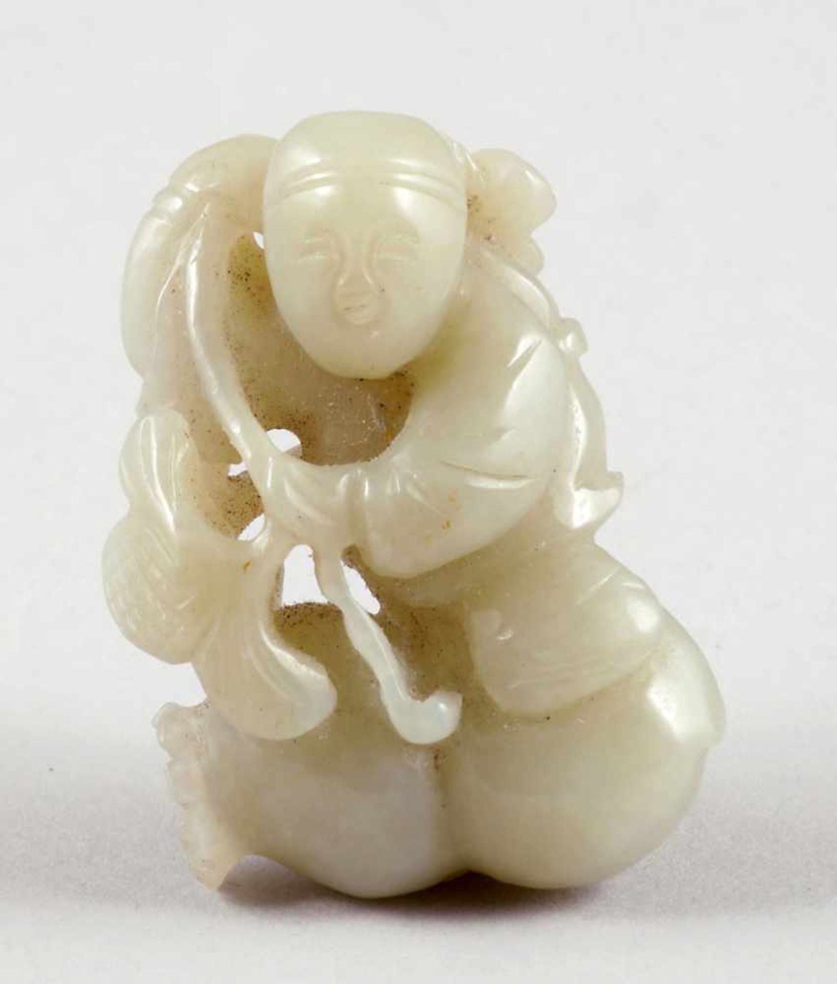 Jadeschnitzerei als Kind mit FrüchtenChina, 19. Jahrhundert. Jade. L. 6,5 cm. Gew. 60 g.