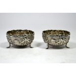 A pair of Indian silver salt pots, decorated with huts and palms