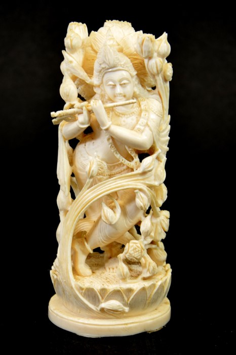 λ A 19th century Indian carved ivory figure of a deity playing the pipe