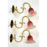 Three Arts and Crafts wall mounted brass lights, with opalescent and cranberry glass shades