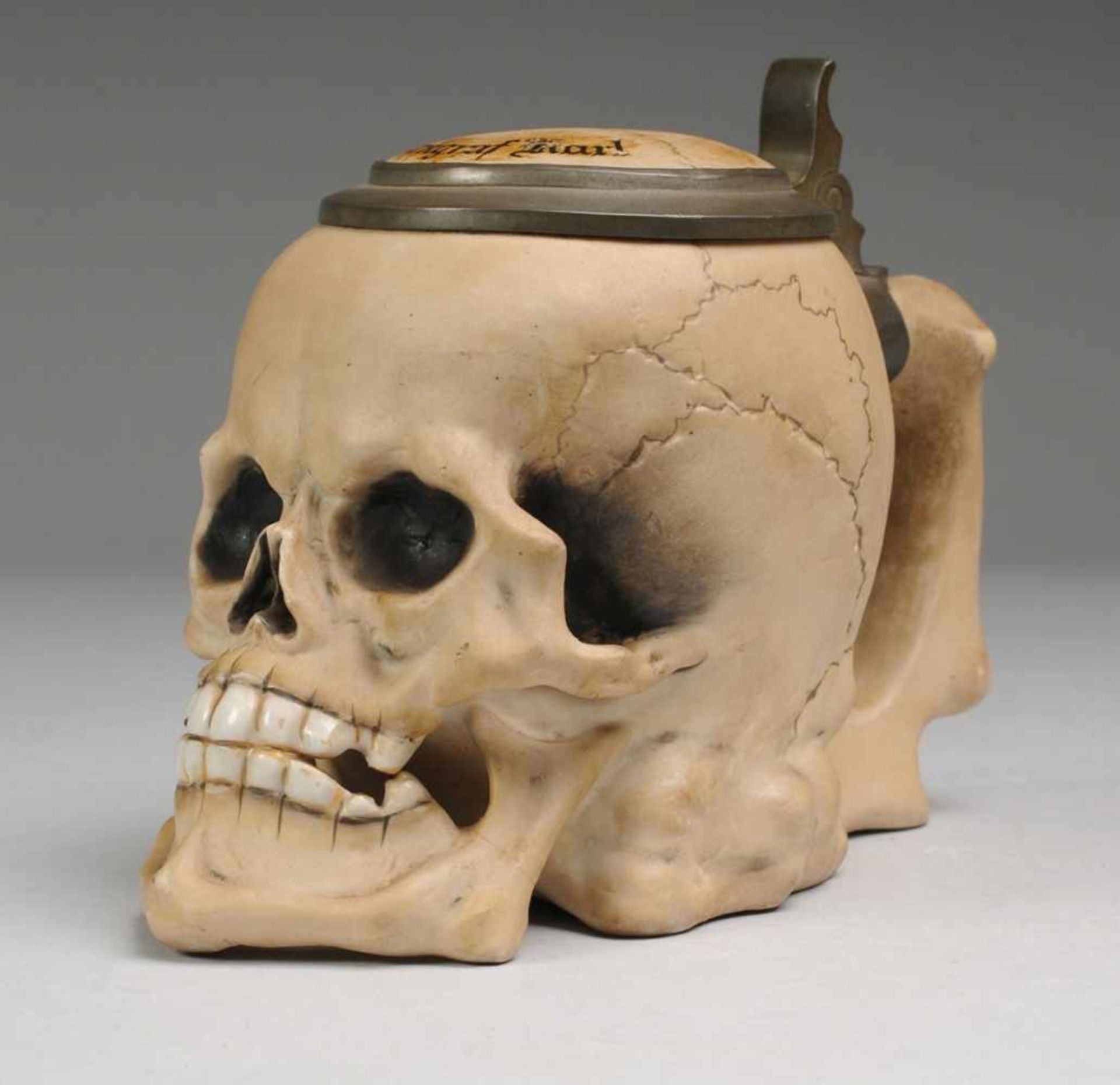 Totenkopf-Bierkrug Biskuitporzellan. Krug in Form eines auf Knochen liegenden Schädels. Griff in