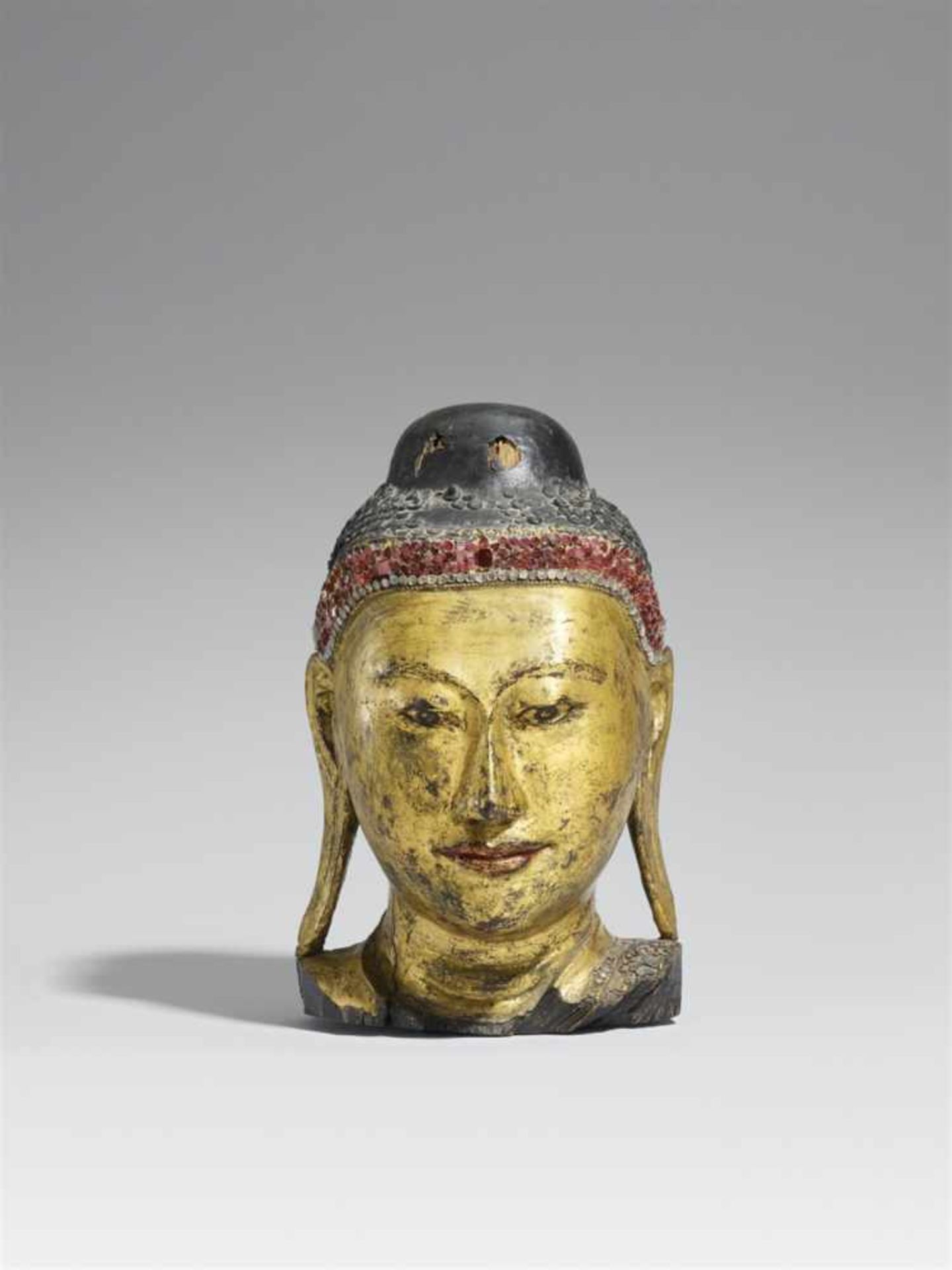 Kopf eines Buddha. Holz, vergoldete Lackfassung und Glassteine. Birma, Mandalay. 20. Jh.Länglicher