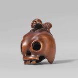 An amusing boxwood netsuke of a skull and a skeleton. Late 19th centuryA skinny skeleton crouches on