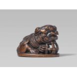 A large wood seal-type netsuke of a shishi. 19th centurySeated on a flat oval base, its chin resting