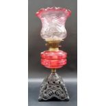 Victorian oil lamp with cranberry blush glass shade and cranberry reservoir over a cast iron base.
