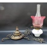 A cast bronze hanging oil lamp with white opaque glass reservoir and cranberry glass shade.