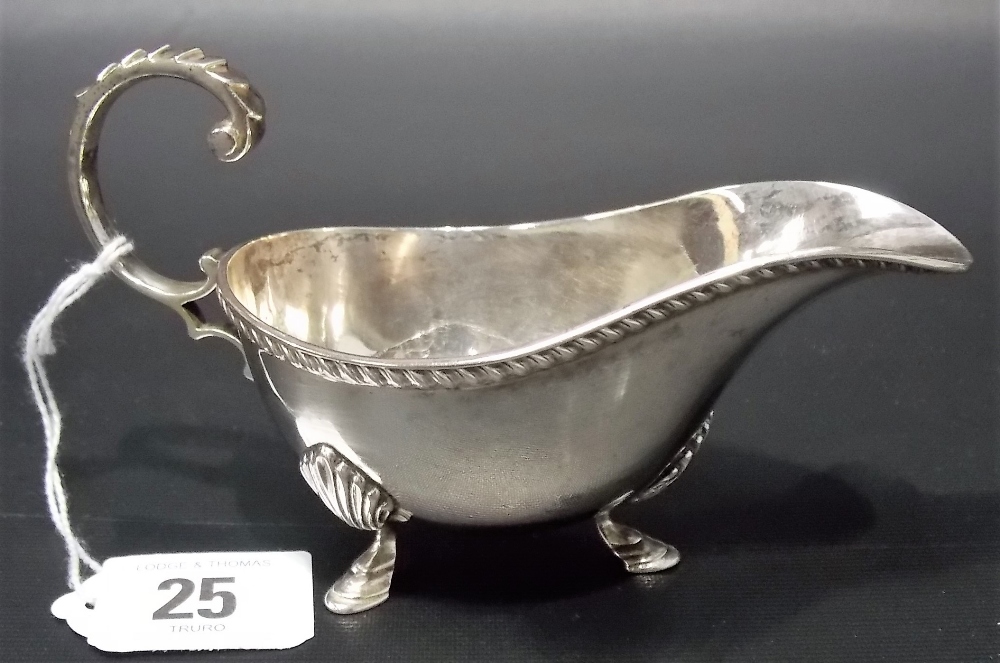 George V silver sauce boat with flying scroll handle, gadrooned rim and on triple feet, Birmingham