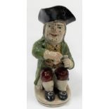 An early 19th Century 'sinner' toby jug, wearing a green jacket over a patterned waistcoat and