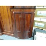 George III mahogany inlaid bow front wall hanging corner cabinet, the frieze with two oval marquetry