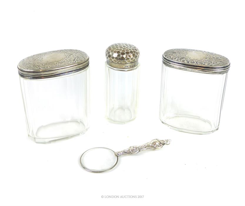 Three silver lidded and cut glass dressing table containers and magnifying glass