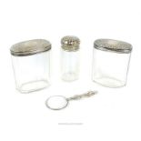 Three silver lidded and cut glass dressing table containers and magnifying glass