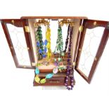 A wooden jewellery cabinet with glass panelled doors and necklaces within