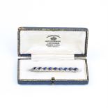 A boxed, Art Deco, white gold and platinum, sapphire and diamond bar brooch