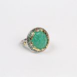 An 18 ct white and yellow gold, large, carved, circular, emerald ring