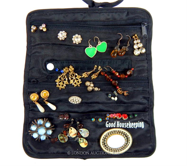 A black satin jewellery roll containing numerous pairs of earrings