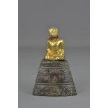 An Asian wooden Buddha covered with a layer of gold and silver on a wooden stand. 12 cm tall.