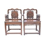 A pair of Chinese late Qing dynasty hardwood armchairs carved with a central back panel depicting va