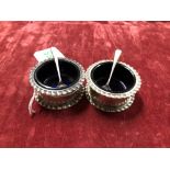 A pair of silver salts with blue glass liners with two silver spoons.