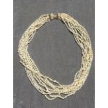 A nine string seed pearl choker style necklace with gold and diamond ribbon shaped clasp.
