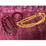 An amber coloured bangle and two strings of amber coloured beads.