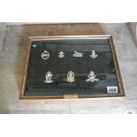 MILITARIA - A framed cap badge display produced by