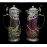 A pair of Continental pewter mounted glass claret jugs, the metal formed as Art Nouveau floral