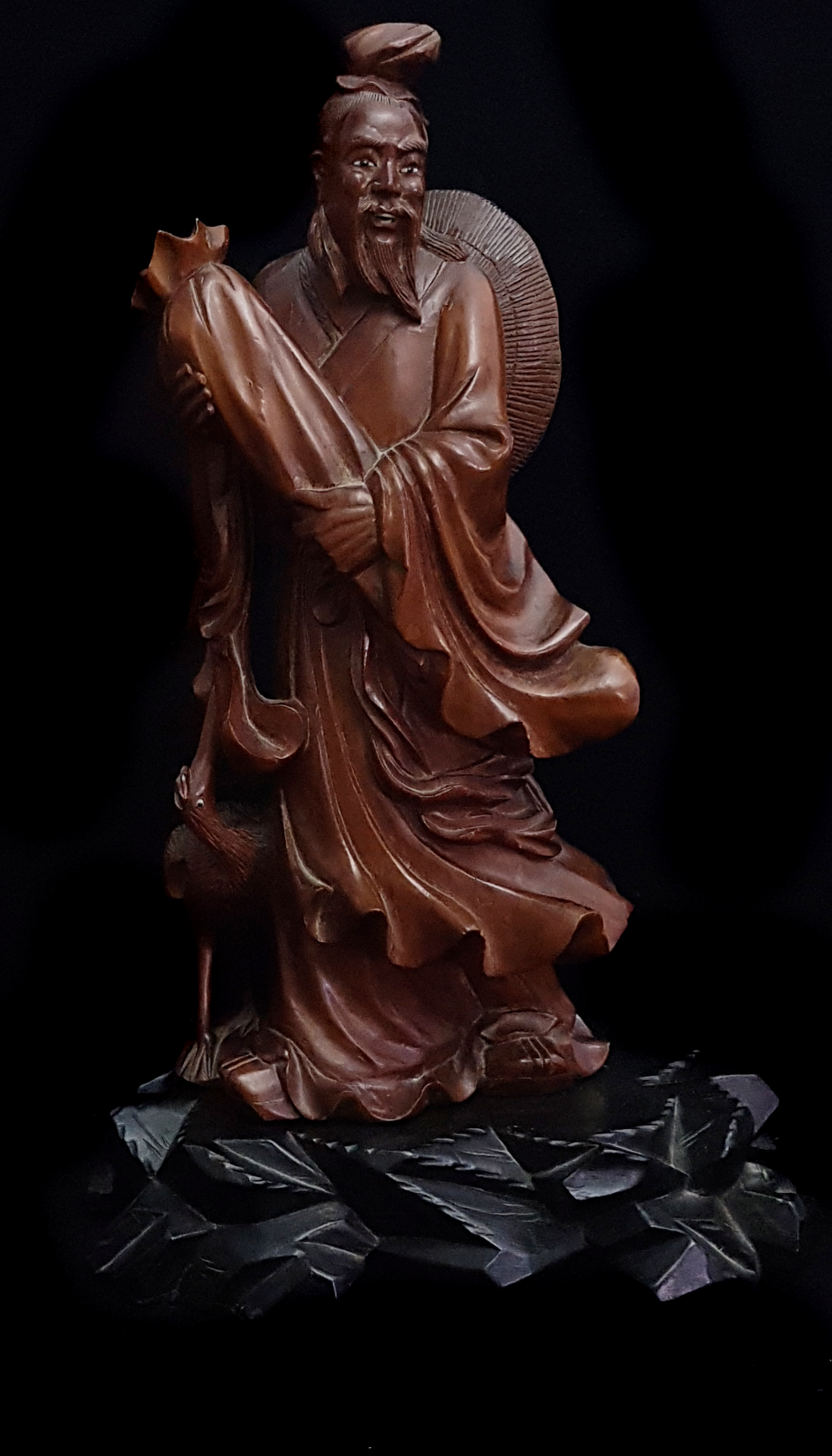 A Chinese bamboo carving of an immortal holding a large wrapped scroll, a crane to one side, eyes