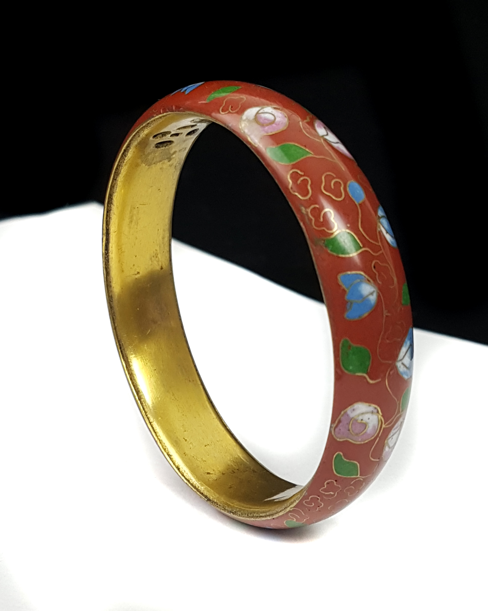 A Chinese cloisonne bangle decorated with a continuous floral garland on a claret ground, gilded