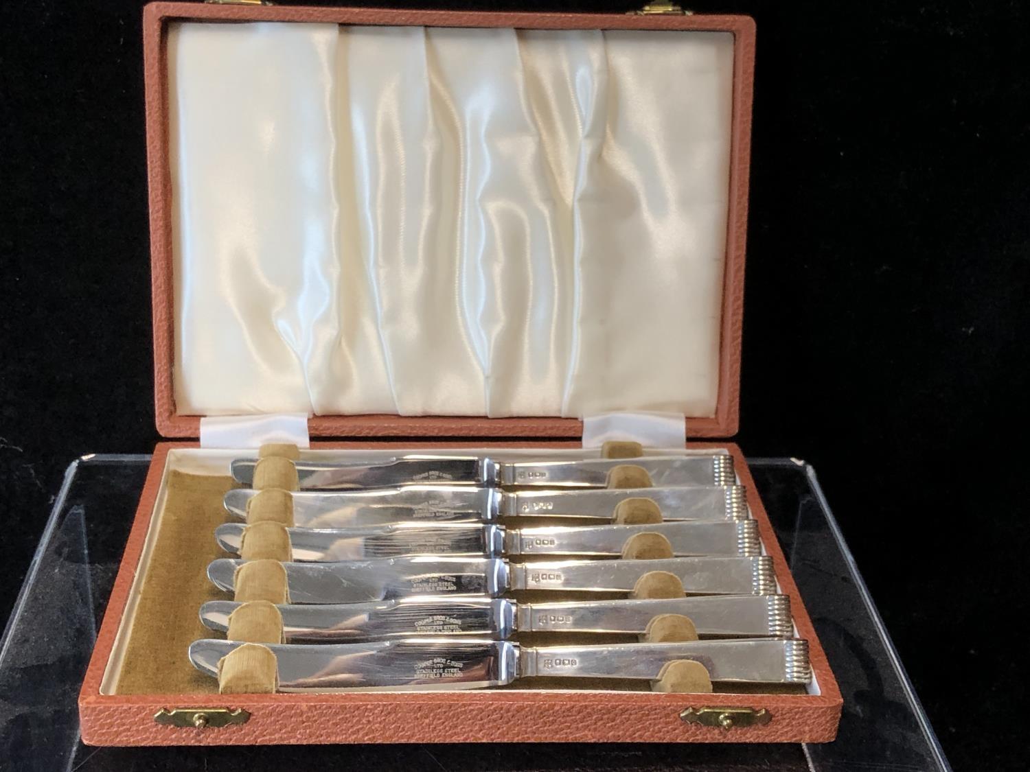 A cased set of six silver handled butter knives, stylised reeded pistol handles, stainless steel