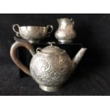 A white metal tea service, probably Indian, the bullet form teapot repousse decorated with flowers