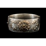 A LATE VICTORIAN HINGED BANGLE, hollow wide two piece bangle with raised gold floral pattern.
