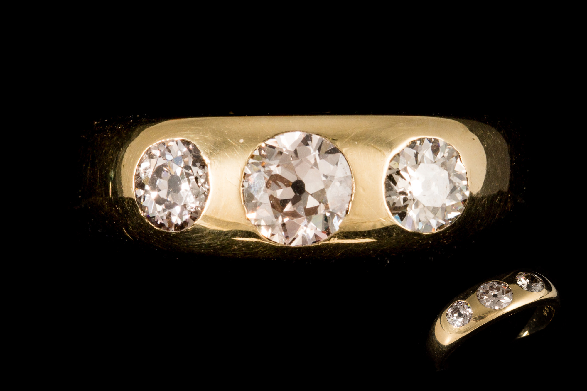 AN ANTIQUE THREE STONE DIAMOND RING, the old cut diamonds gypsy set in 18ct yellow gold.