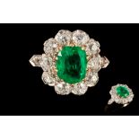 AN EMERALD AND DIAMOND CLUSTER RING, the oval cut emerald weighing 1.