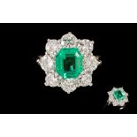 AN EMERALD AND DIAMOND CLUSTER RING, the rectangular cut emerald weighing 1.