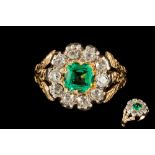 AN EMERALD AND DIAMOND CLUSTER RING, the cushion cut emerald of approximately 0.