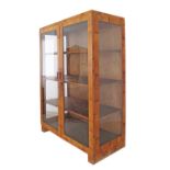 An Art Deco revival blonde walnut veneered display unit with two doors enclosing solid wood shelves.