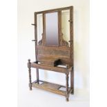 An English carved solid oak entrance hall stand with central mirror, hat and coat pegs and