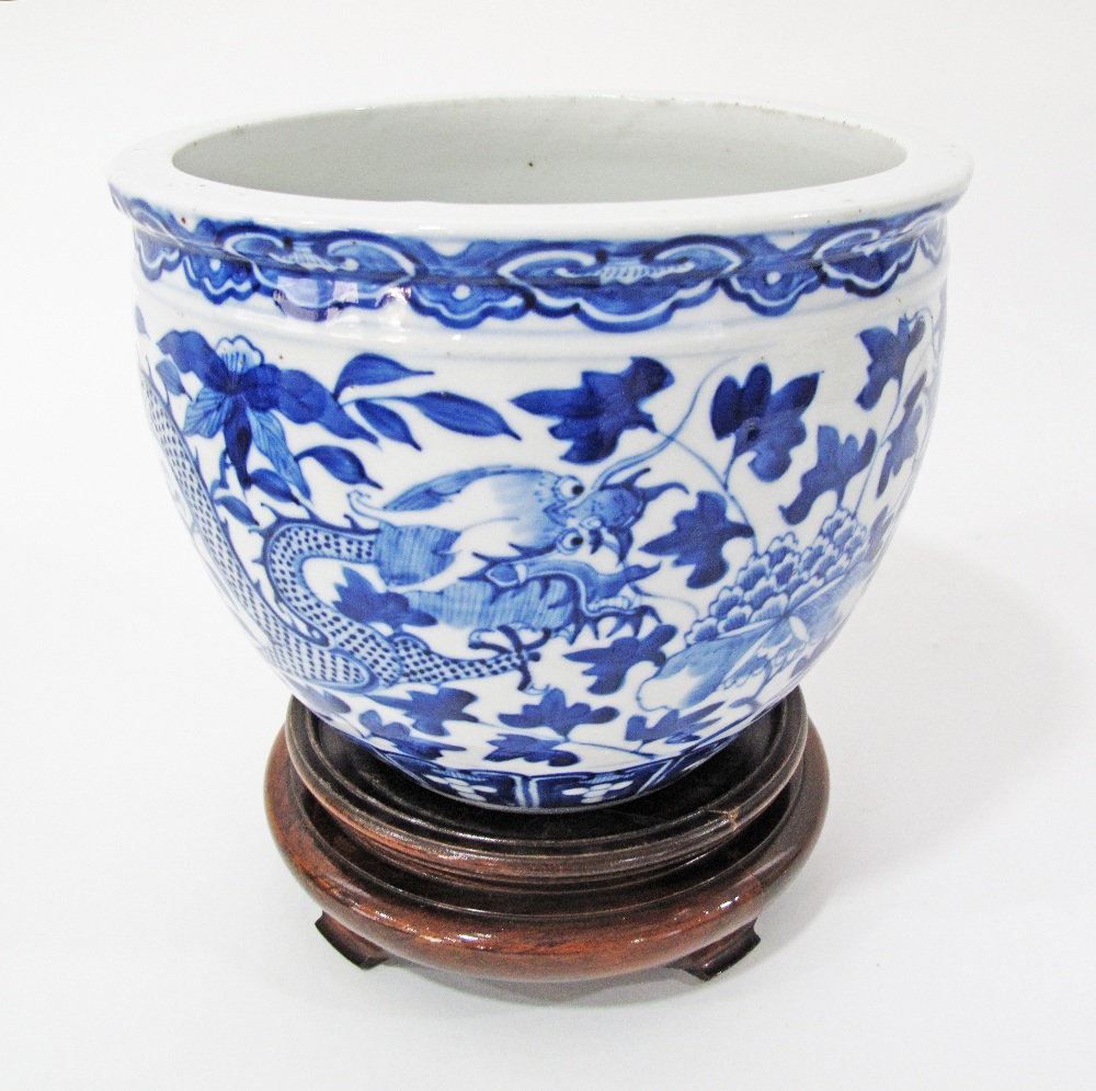 A Chinese blue and white porcelain fish bowl with dragon and leaf decoration on hardwood stand