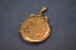 A late Victorian yellow metal pendant locket, circular, the case engraved with seed pearls, rubies