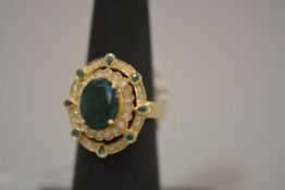 An emerald and diamond cluster ring, the central oval-cut emerald claw-set above two concentric