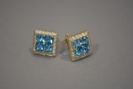 A pair of blue topaz and diamond cluster earrings, each set with four square-cut topaz within a band