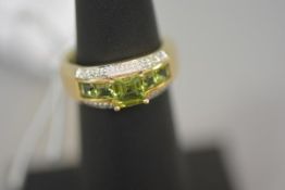 A peridot and diamond ring, centred by a square cut peridot between two pairs of smaller square-