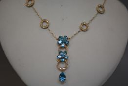 A striking blue topaz and diamond pendant, designed as twin flowerheads spaced by diamond set